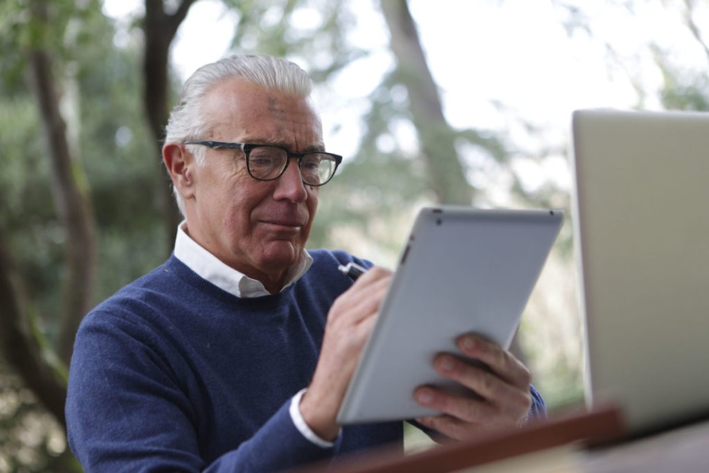 An elderly man writing on a tablet device.