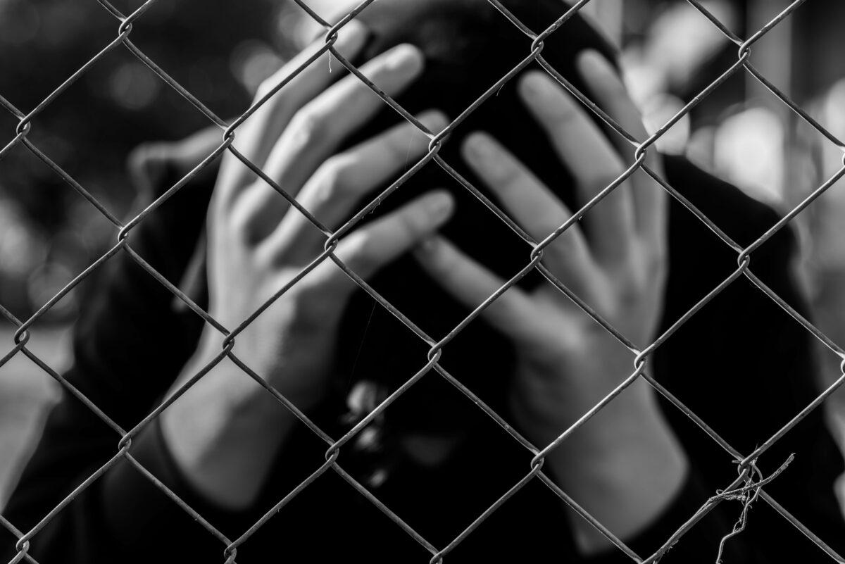 Worried man sitting behind a chain-link fence