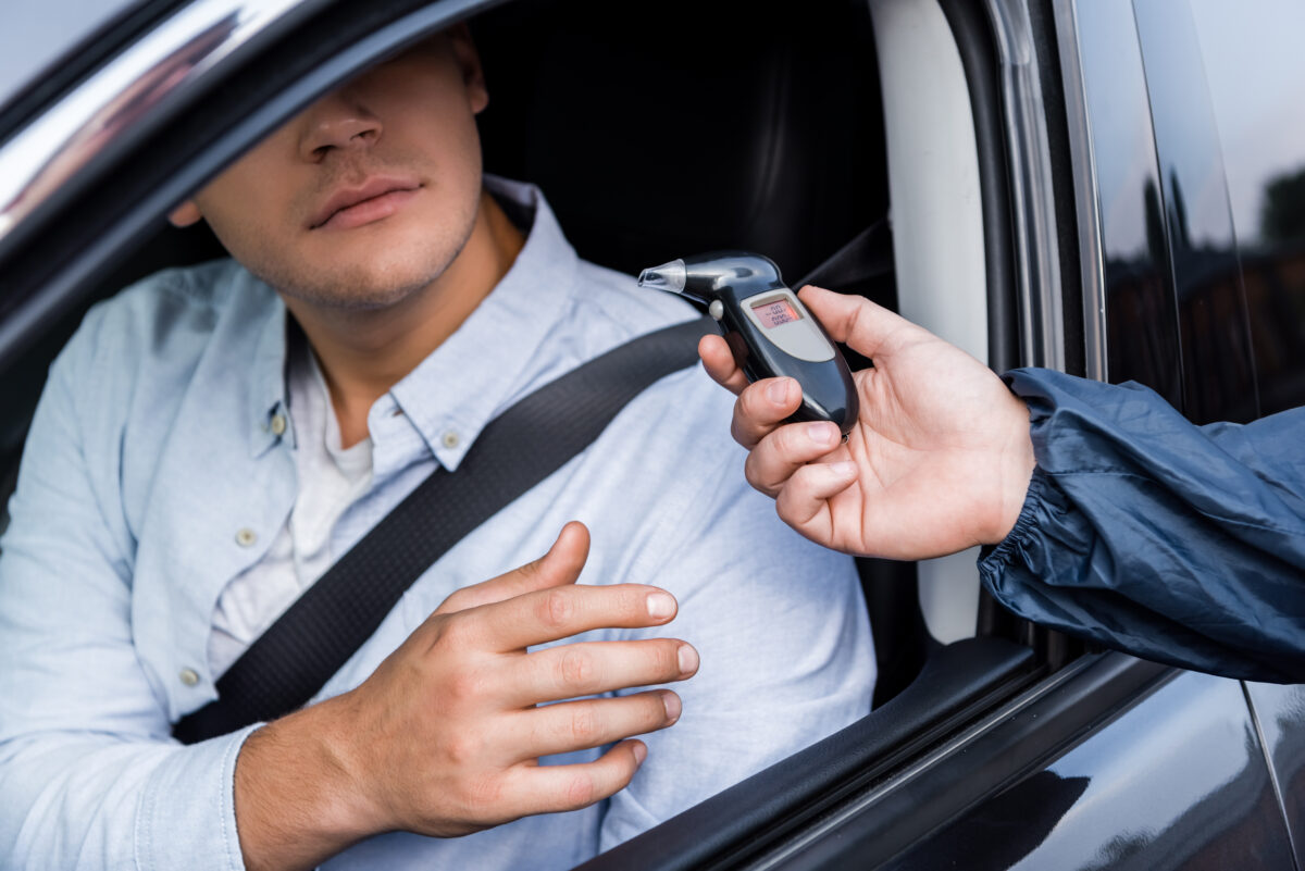 cropped view of driver taking breathalyzer from a policeman while sitting in a car