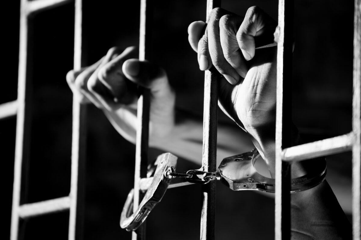 person in handcuffs behind bars