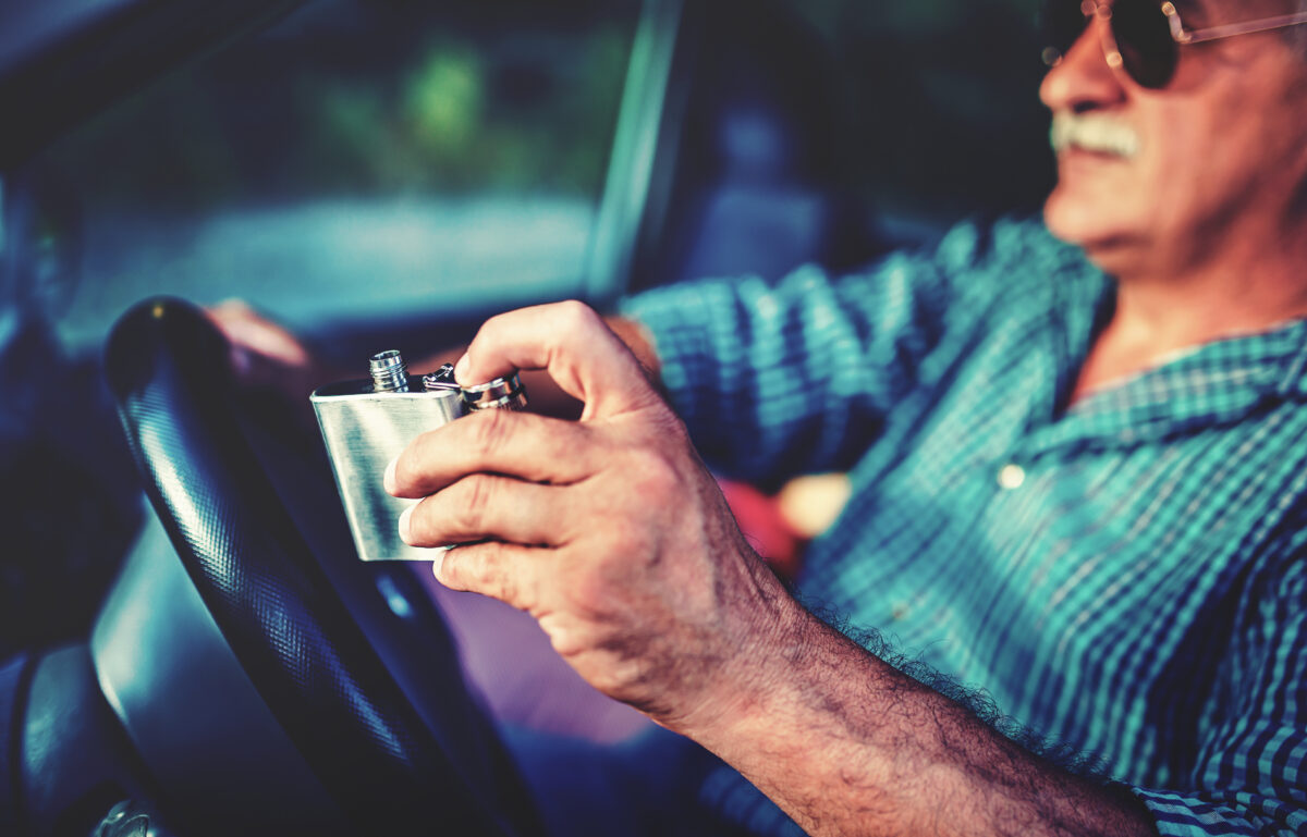 A photo of an elderly man drinking liquor while driving.