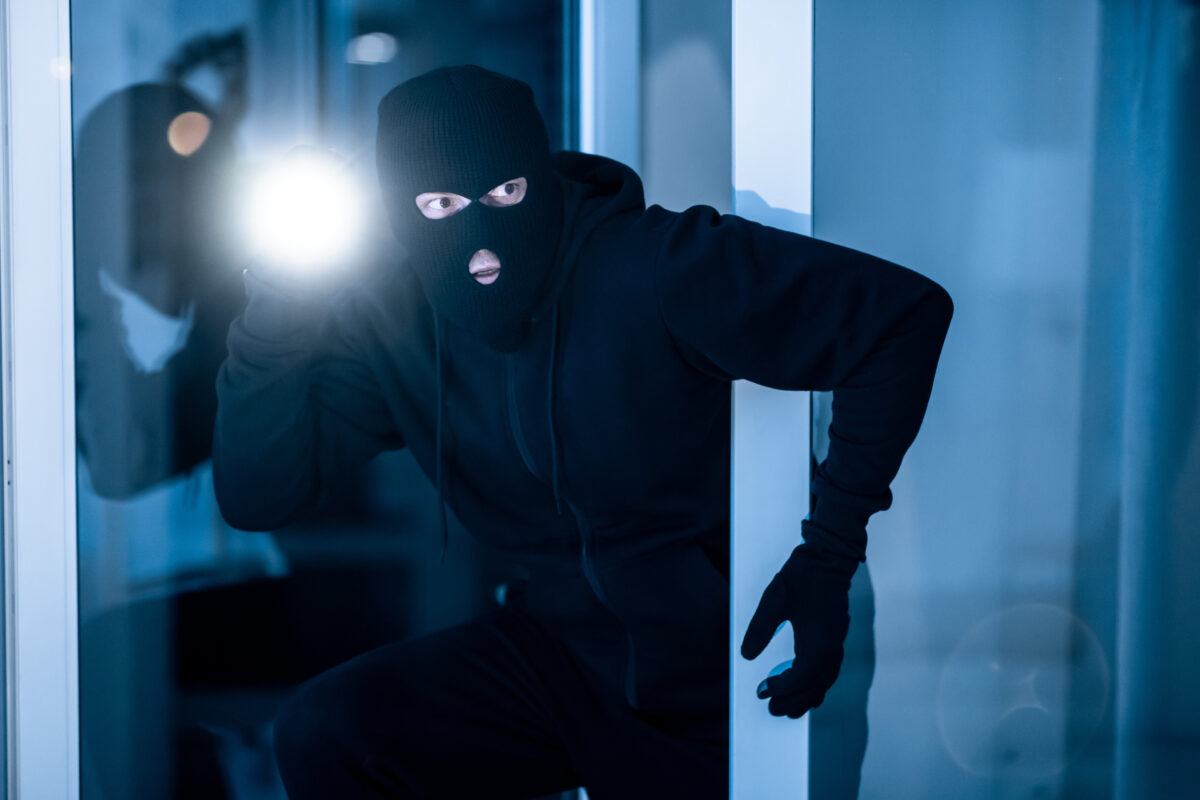 Cautious burglar looking and peeping into building through window or glass door with torch.