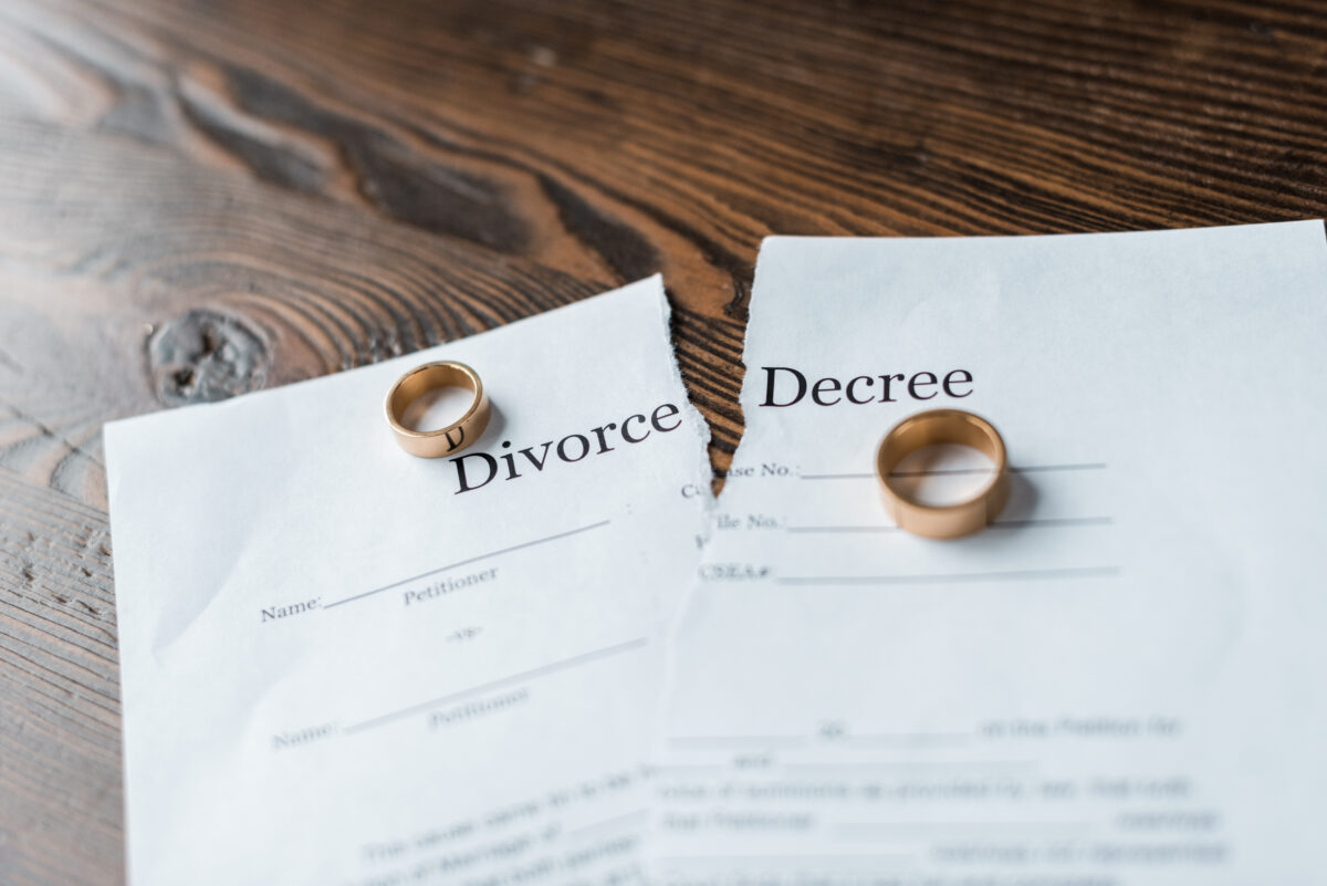 close-up shot of teared divorce decree and engagement rings on a wooden surface