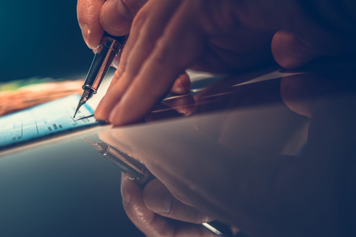 Caucasian Men Writing Check Using Fountain Pen on Reflective Desk.