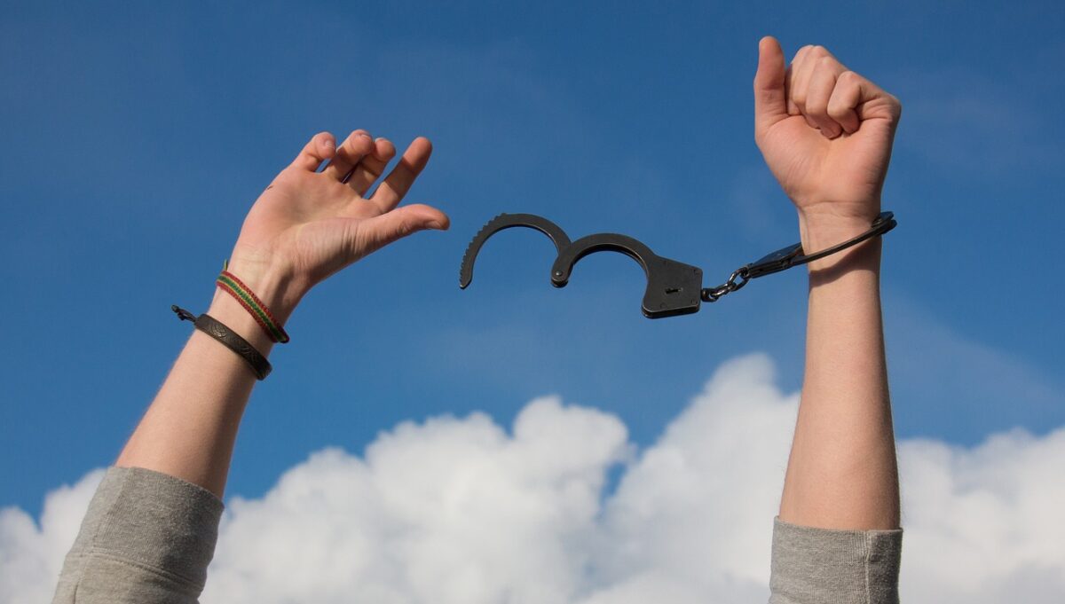 An image of a young man with one hand in handcuffs, set against an outdoor landscape symbolizing freedom.