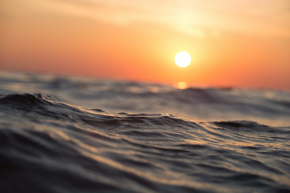 An image of ocean waves with the sun setting in the background.