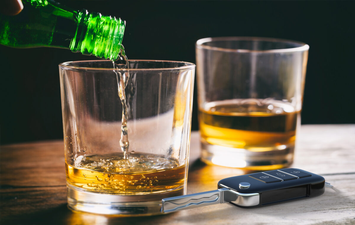 Drinking and driving concept. Car key and whiskey glass and bottle on a wooden bar counter background.