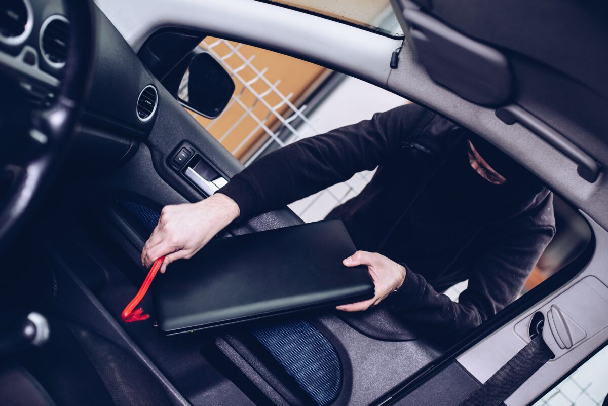 Masked thief in a balaclava stealing laptop computer from car