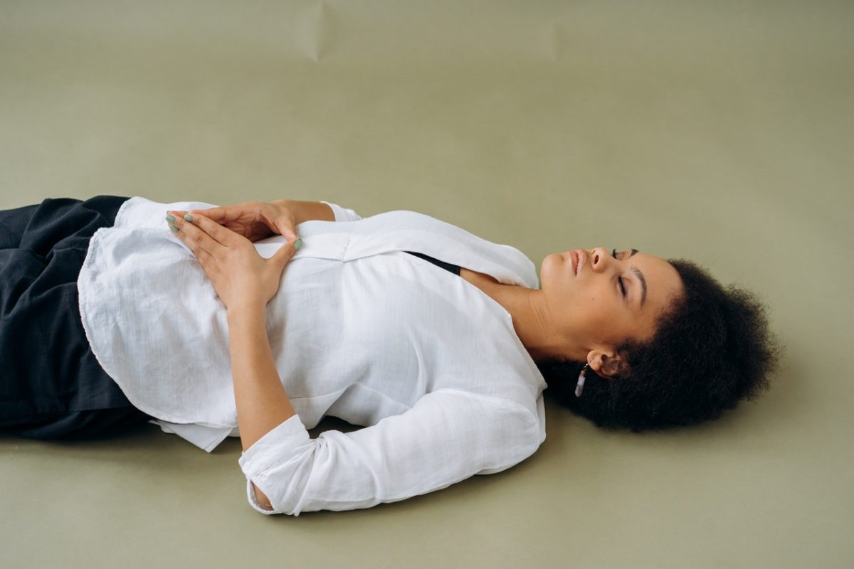 Woman lying on the floor with her hands on her abdomen. She appears to be meditating.