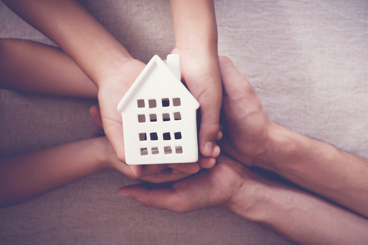 Adult and child hands holding white house, family home and homeless shelter concept