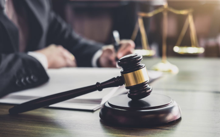 A blurry image of a judge with a scale in the background, and a gavel visible in the foreground.