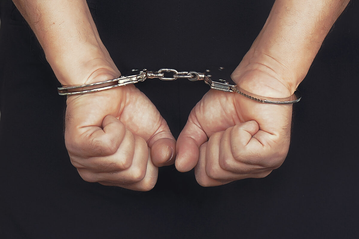 Arrested man handcuffed hands at the back, isolated on a black background.