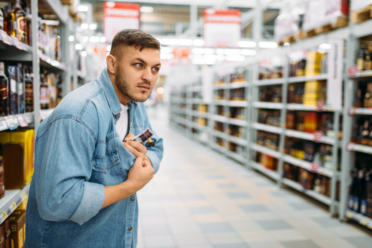 A man hides a bottle of alcohol under his shirt in the supermarket.