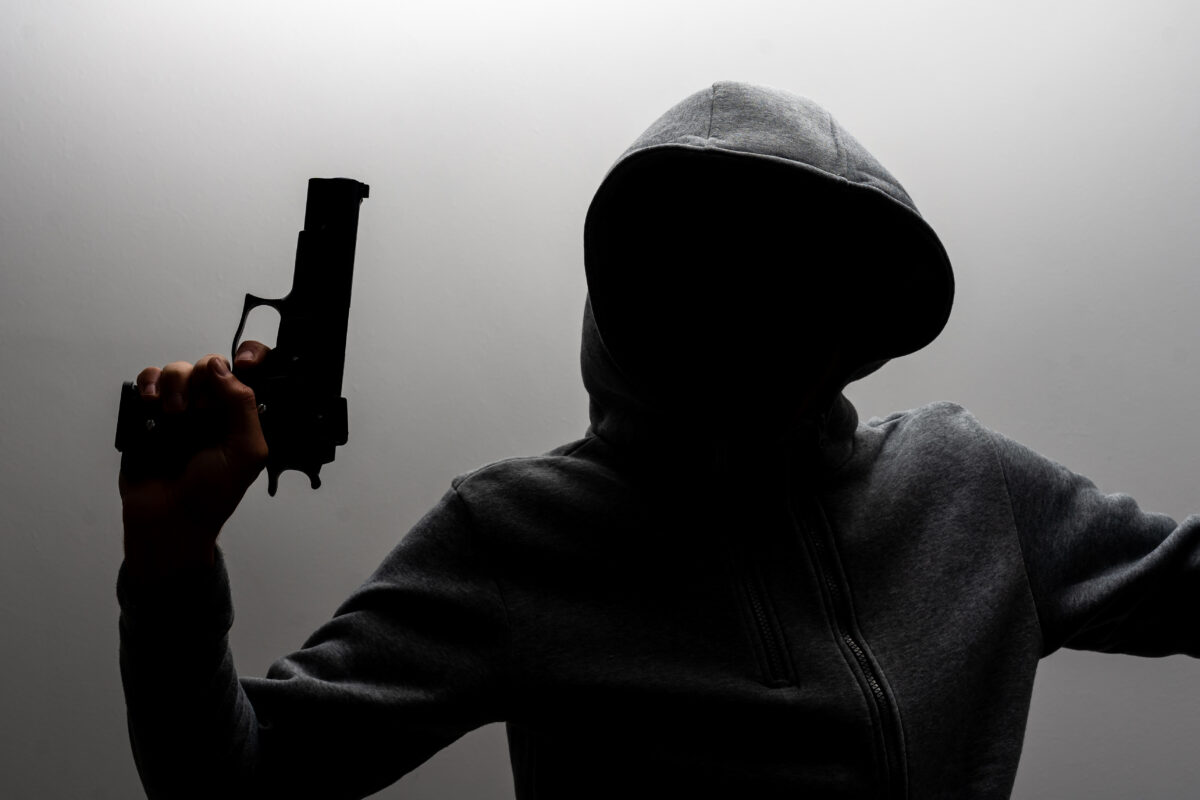 Photo of a creepy horror criminal in black hoodie holding revolver gun