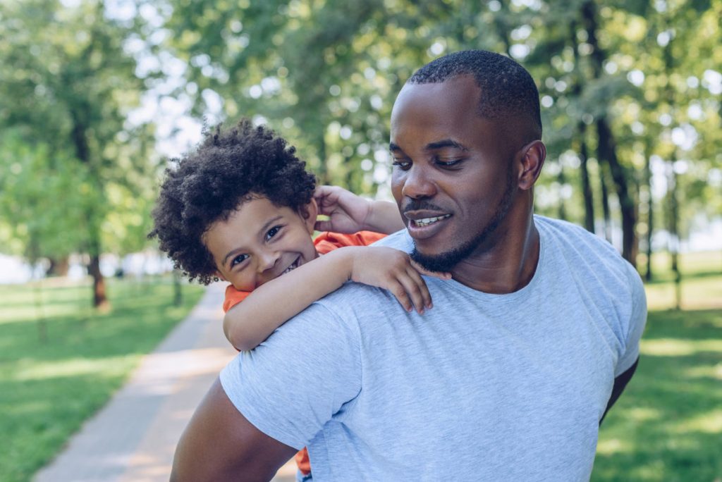 African American man piggybacking cheerful son in the park