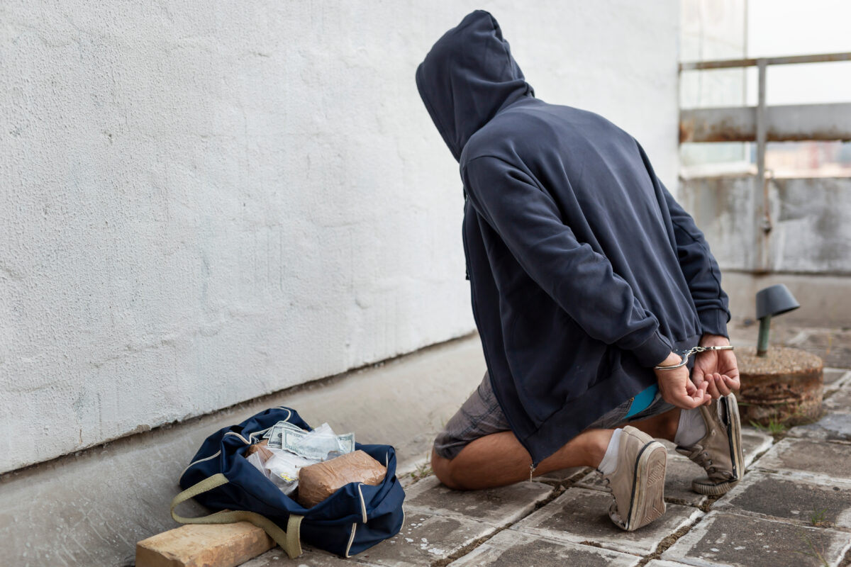 Drug trafficker under arrest confined with handcuffs kneeling on the floor.