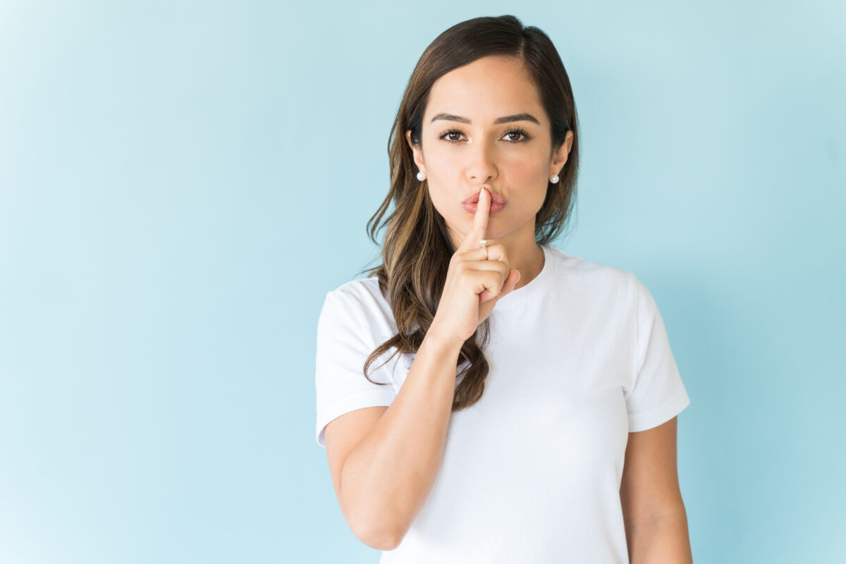 A female with finger on lips standing against colored background