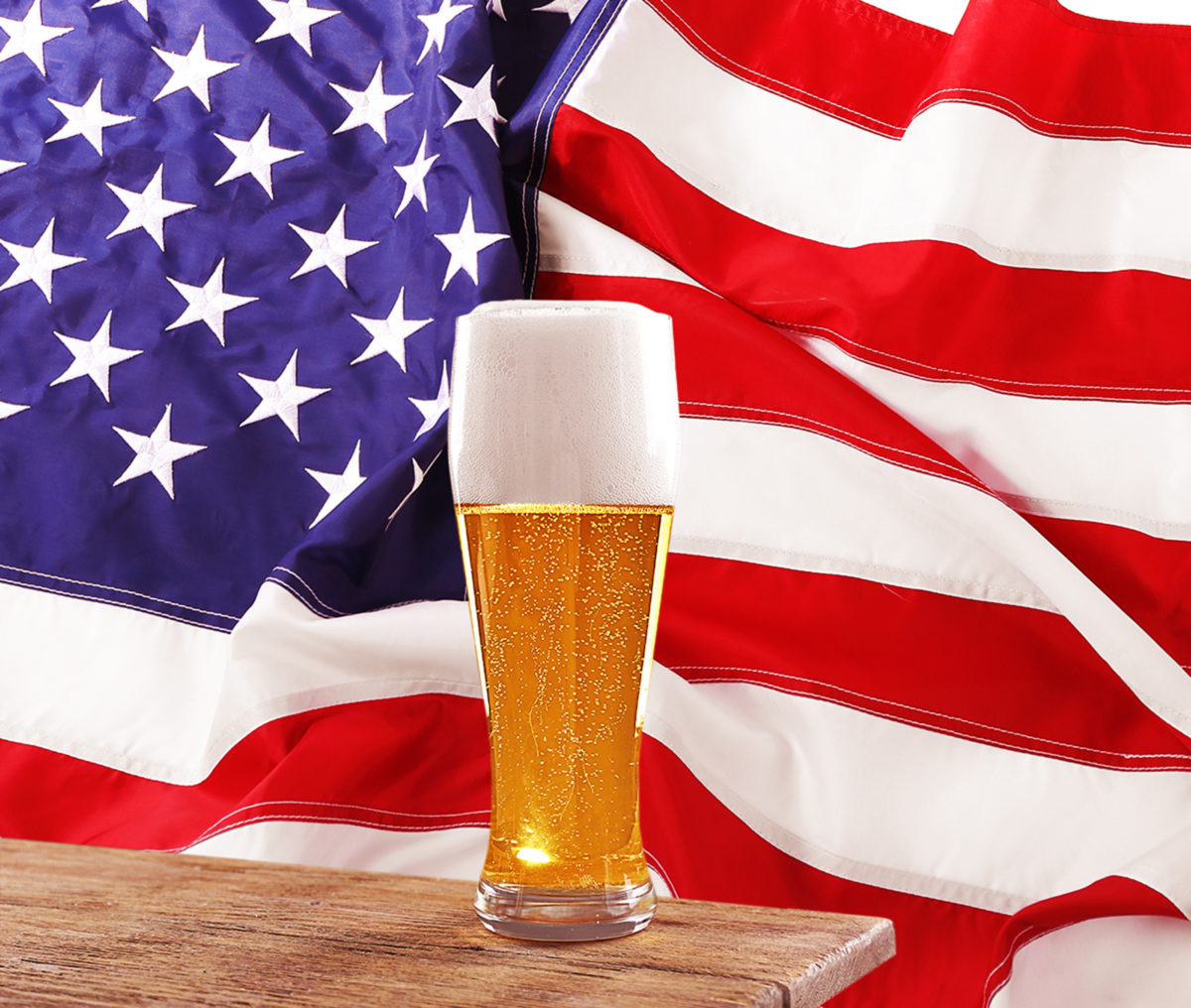 Glass of beer on a wooden table. USA flag background.