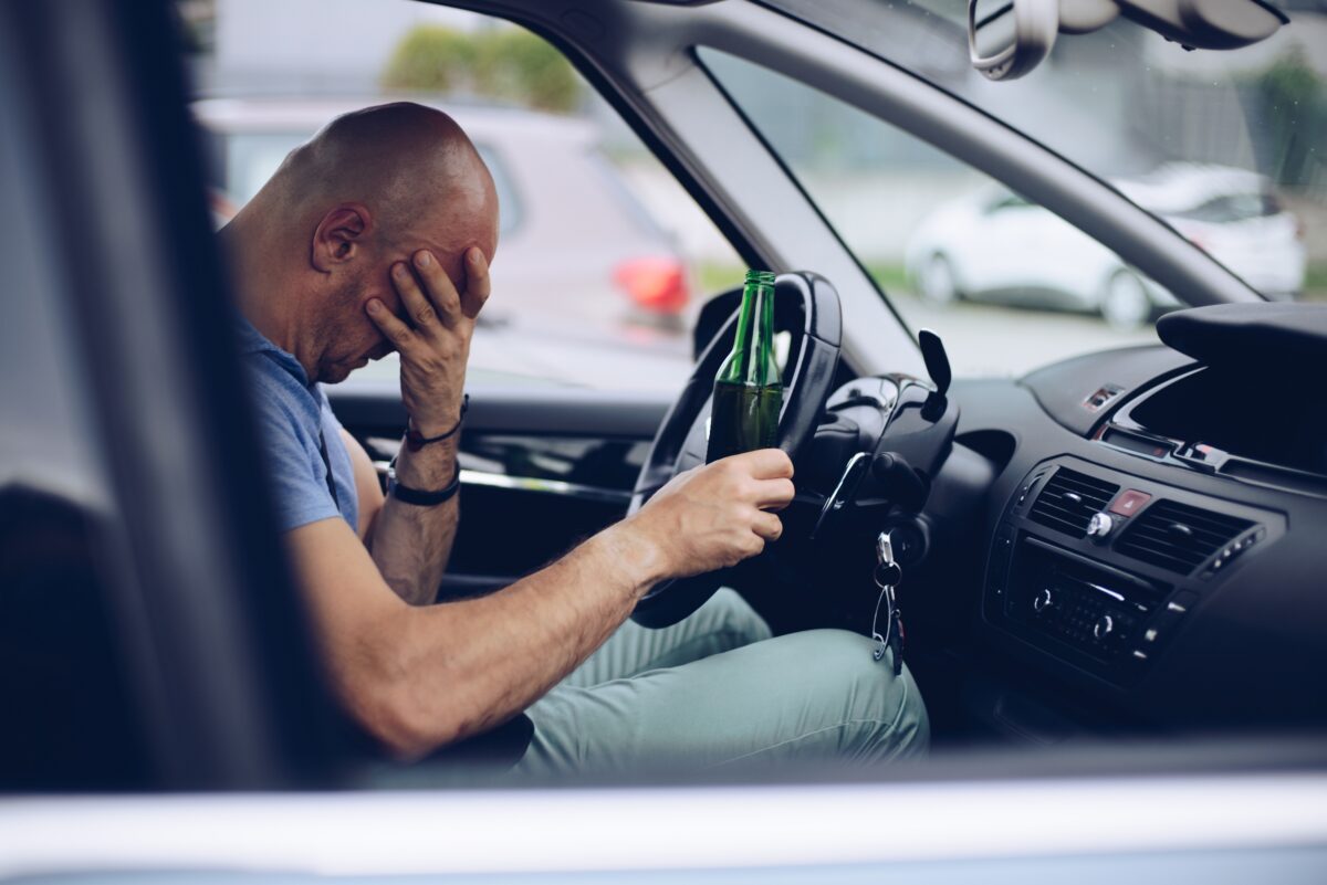 Drunk driver drinking alcohol in car and holding beer bottle